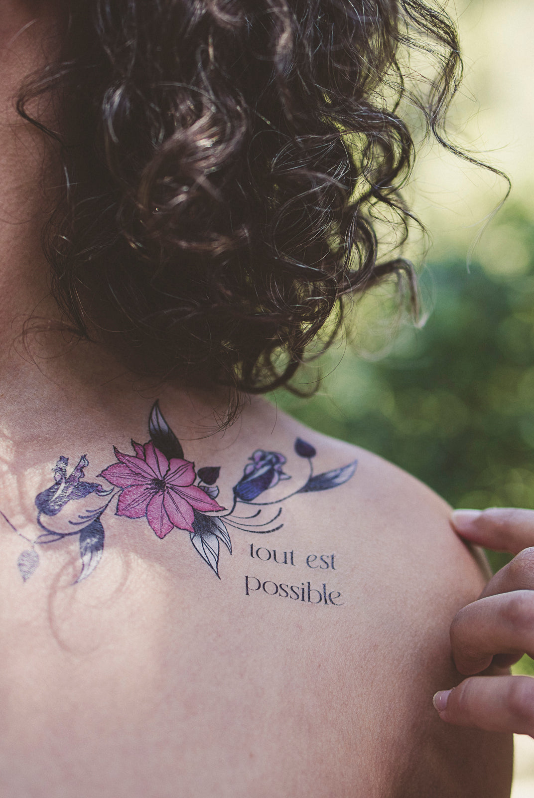 Person wearing a "Tout Est Possible" botanical tattoo on their shoulder as a daily affirmation.