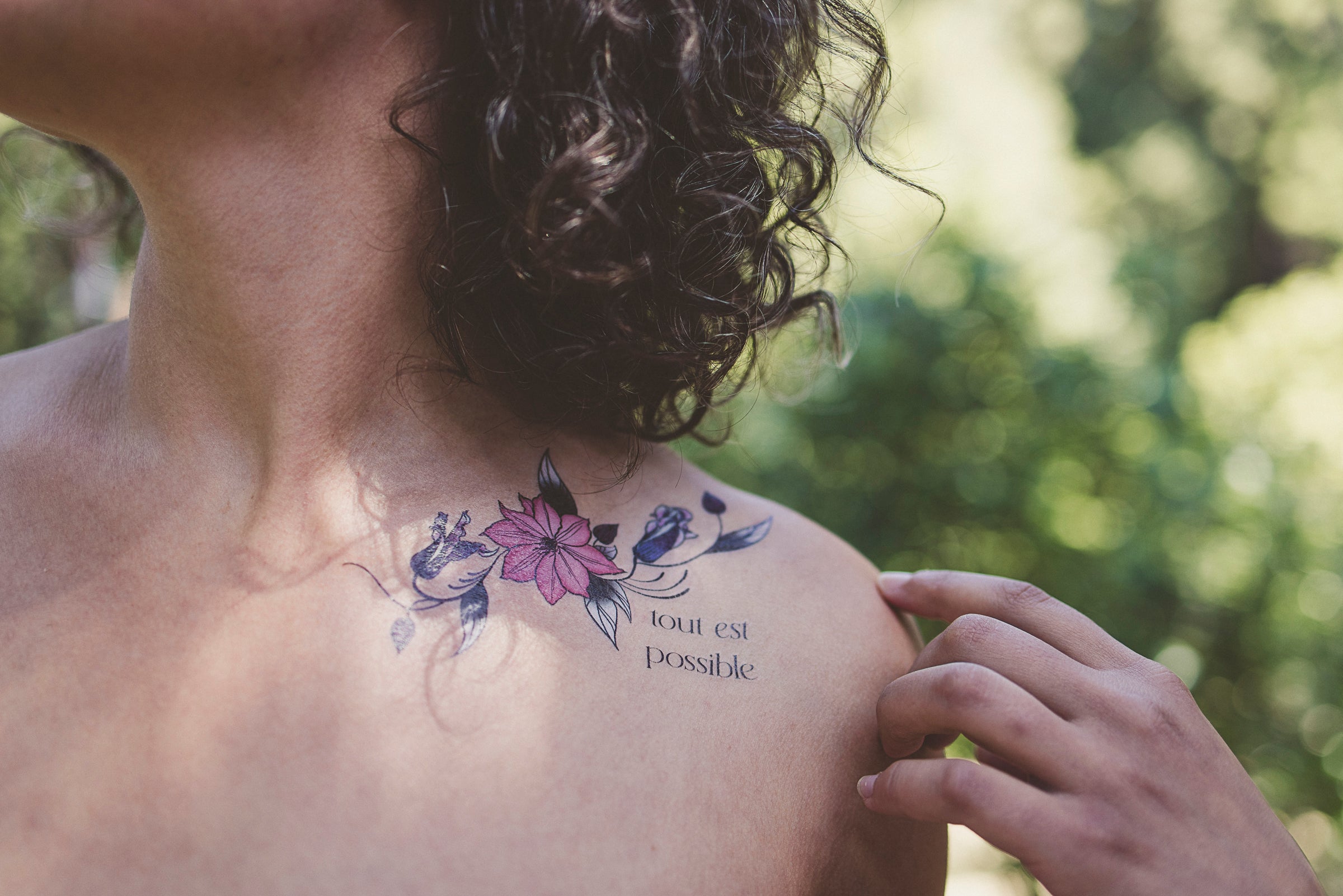 Person wearing a "Tout Est Possible" botanical tattoo on their shoulder as a daily affirmation.