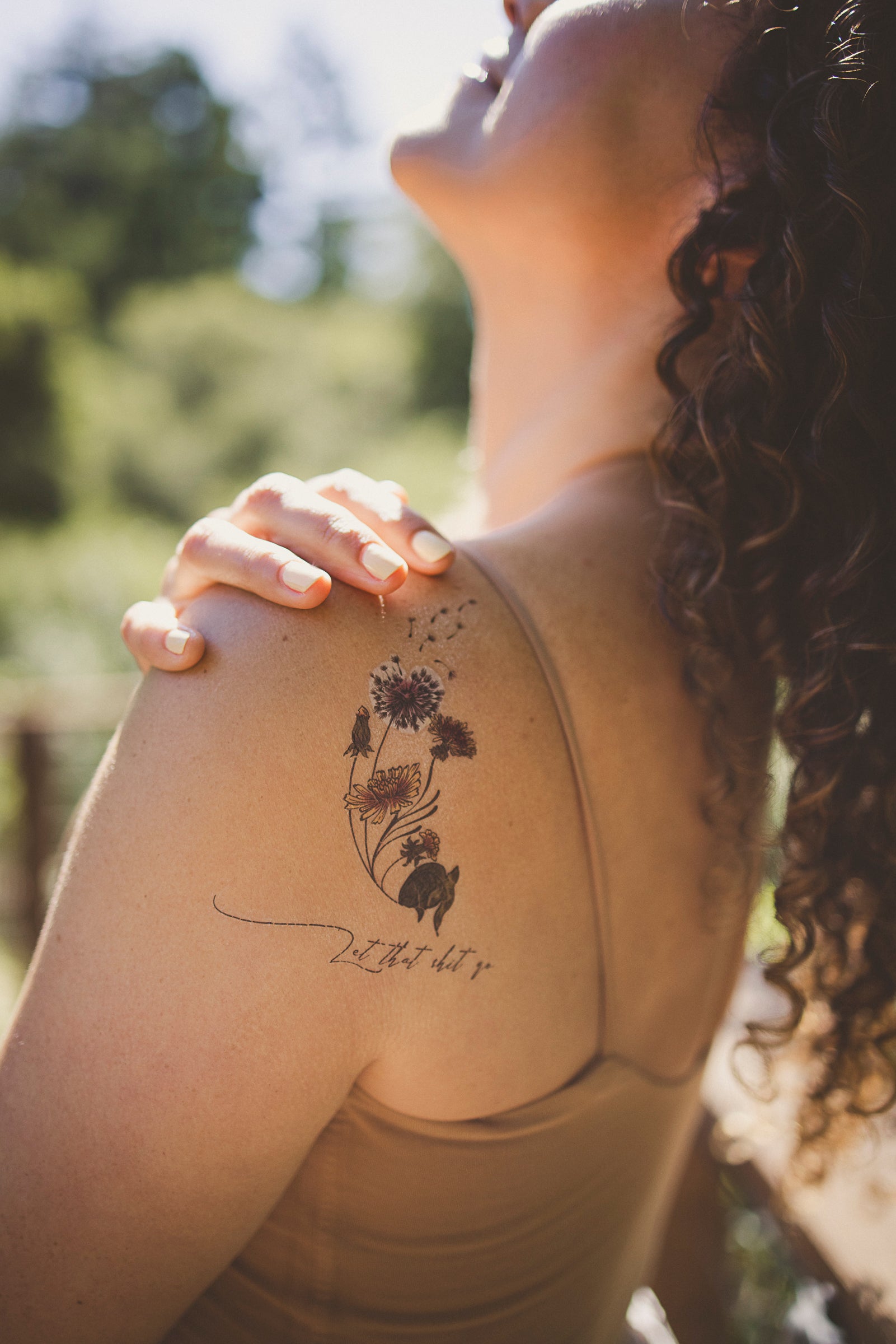 Person wearing a "Let That Shit Go" botanical tattoo on their shoulder as a daily affirmation.