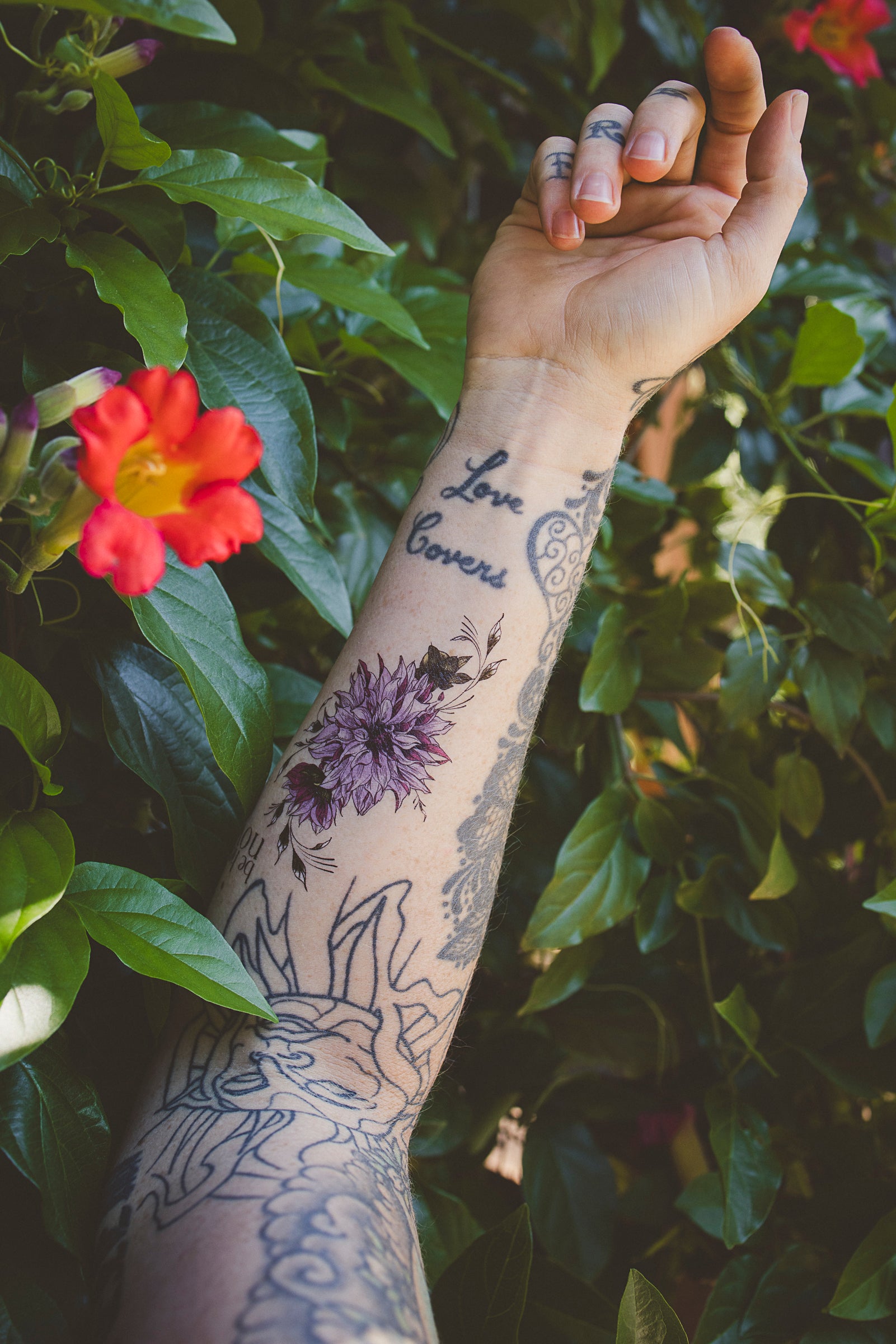 Small botanical temporary tattoo of a dahlia and "Be Here Now" text on inner arm