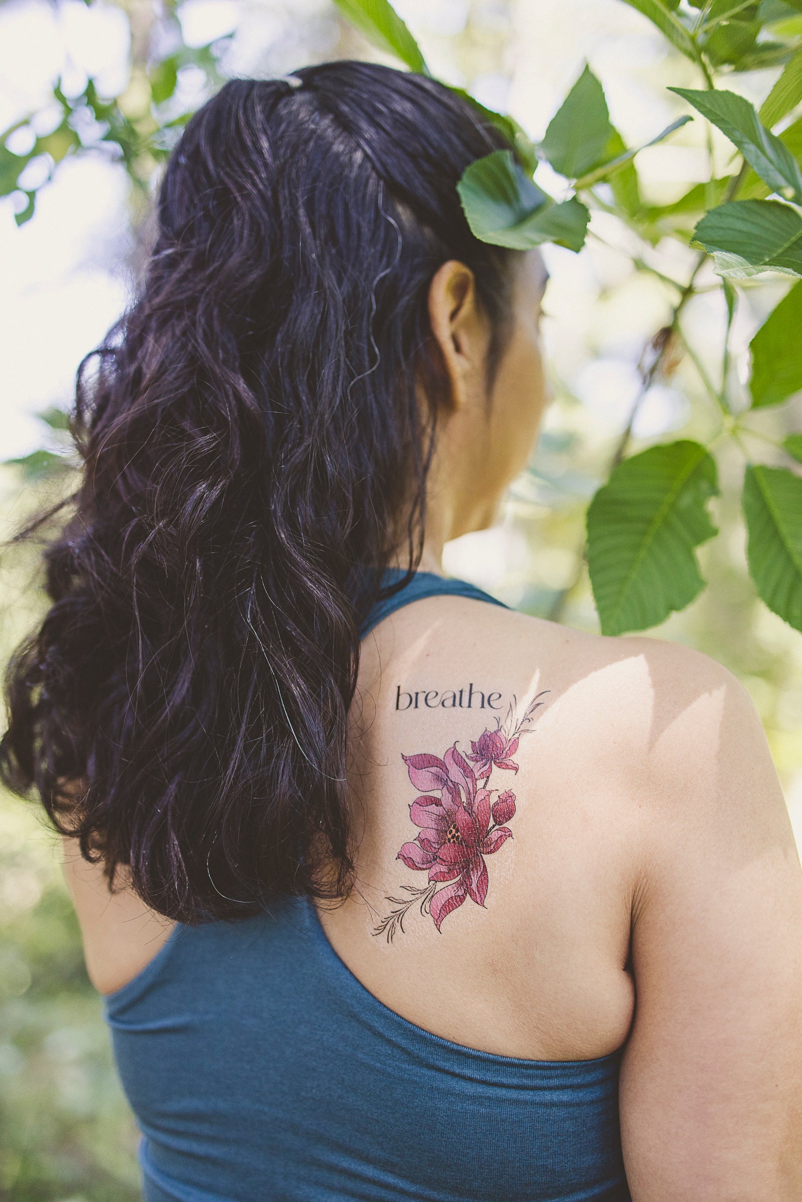 Person wearing a small "Breathe" botanical tattoo on their back