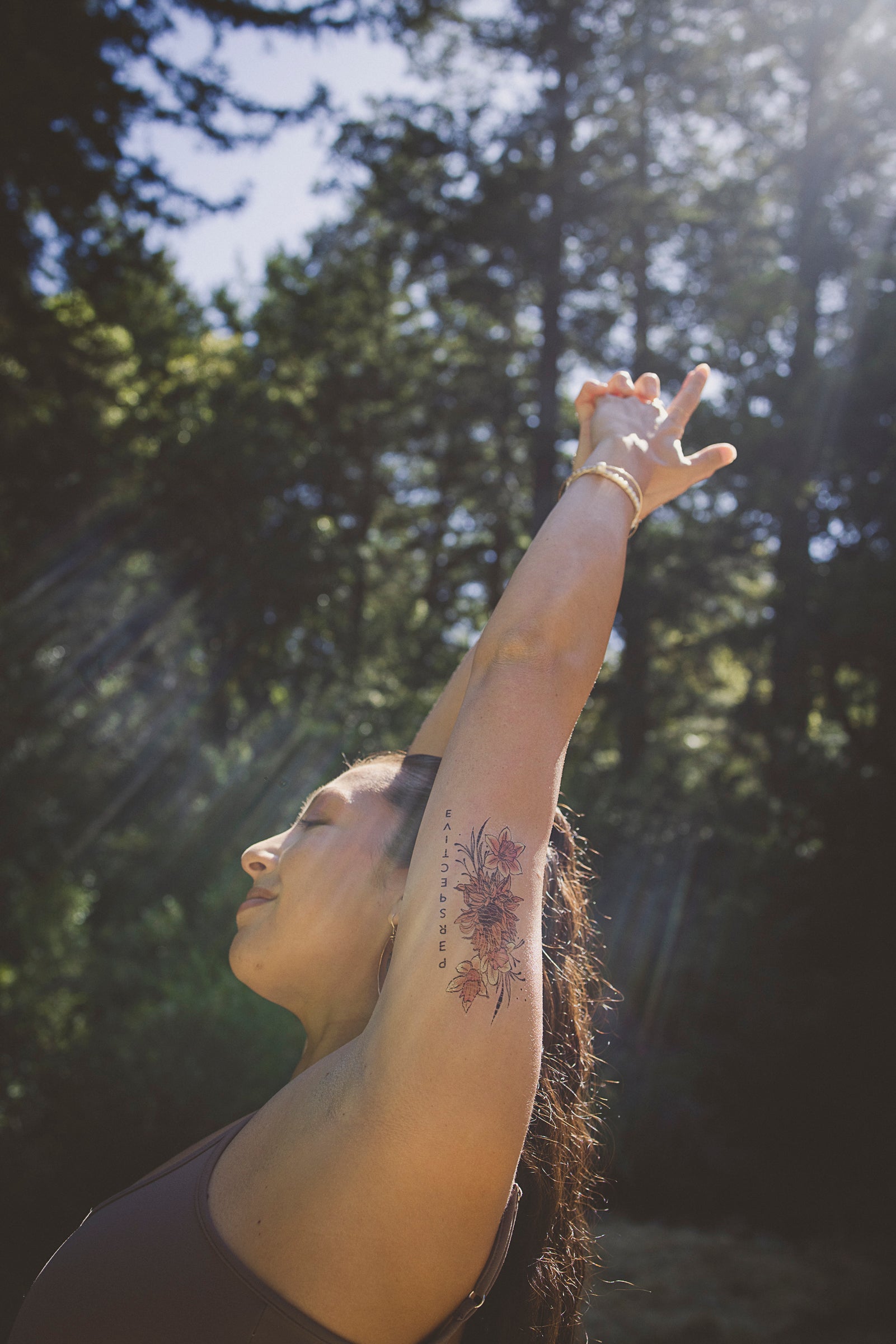 Person wearing a "Perspective" botanical tattoo on their raised arm among nature.